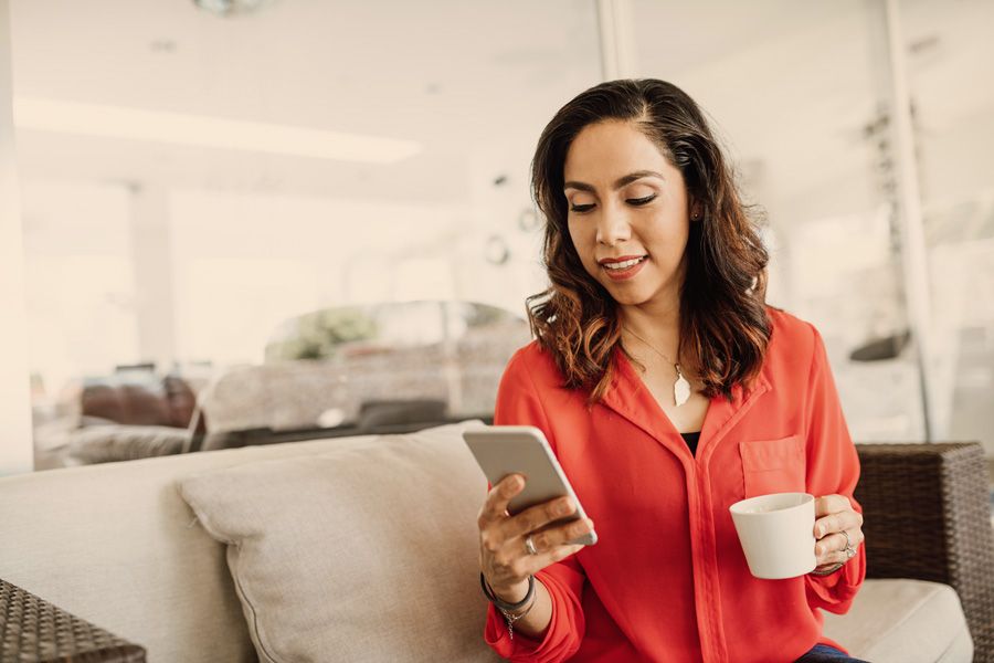 Woman sitting looking at her phone with coffee in her other hand